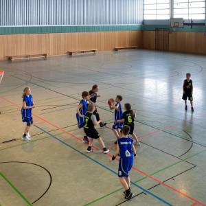 Eine Gruppe von Kindern spielt Basketball in einer Turnhalle.

